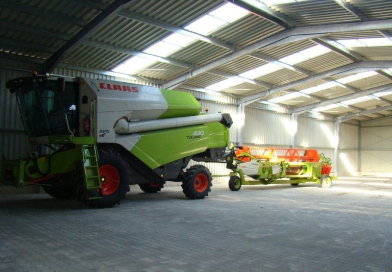 Stalowa hala rolnicza mieszcząca zielony kombajn oraz miejscem na inne maszyny rolnicze