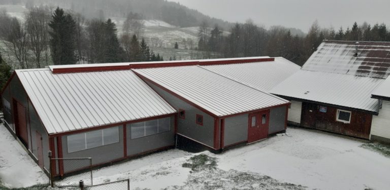 Dach i front szaro-czerwonej hali rolniczej o pow. 420 m2 pokrytej śniegiem