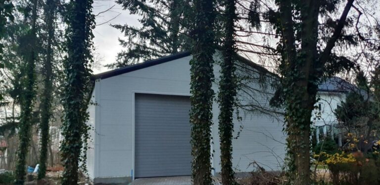 Biały budynek garażowy o pow. 153 m2 z szarą bramą od frontu